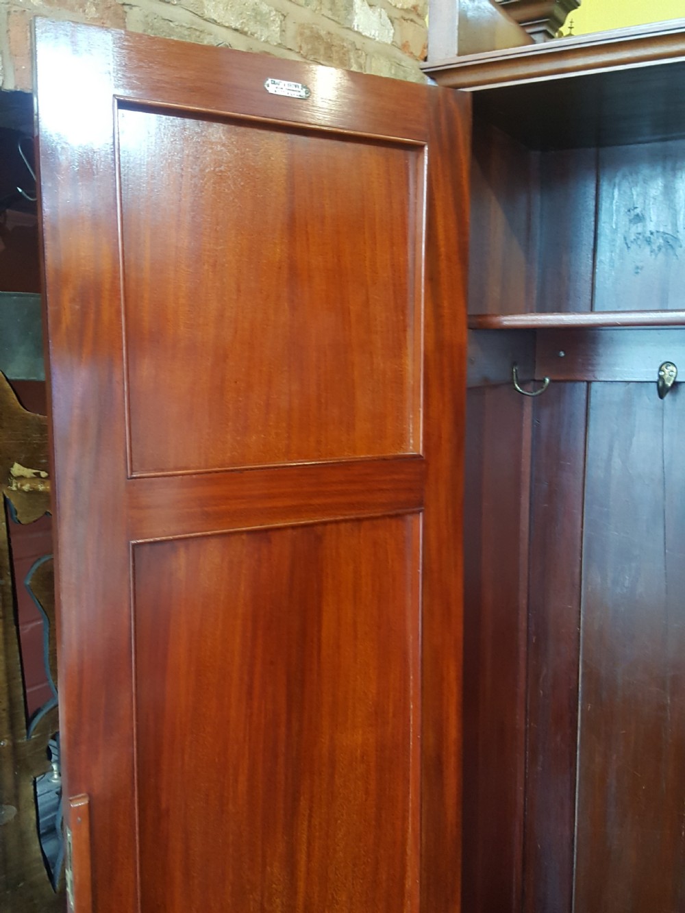 An Arts and Crafts mahogany hall robe featuring carved upper panels, two full-length doors, and a shaped top crest with corner finials. View VII