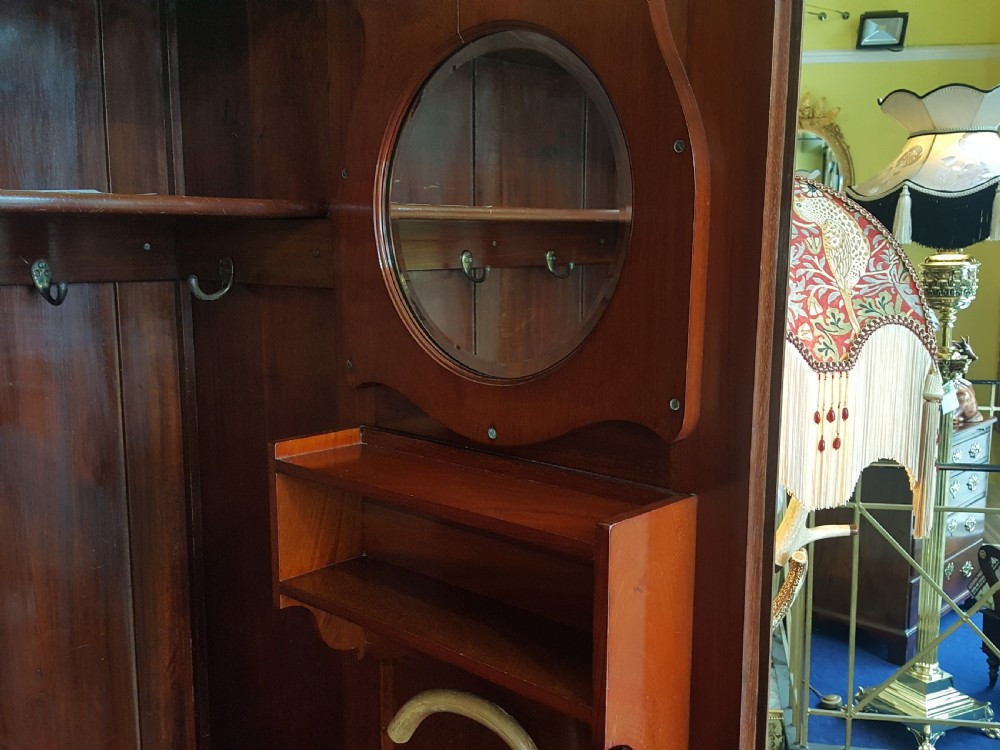 An Arts and Crafts mahogany hall robe featuring carved upper panels, two full-length doors, and a shaped top crest with corner finials. View VIII