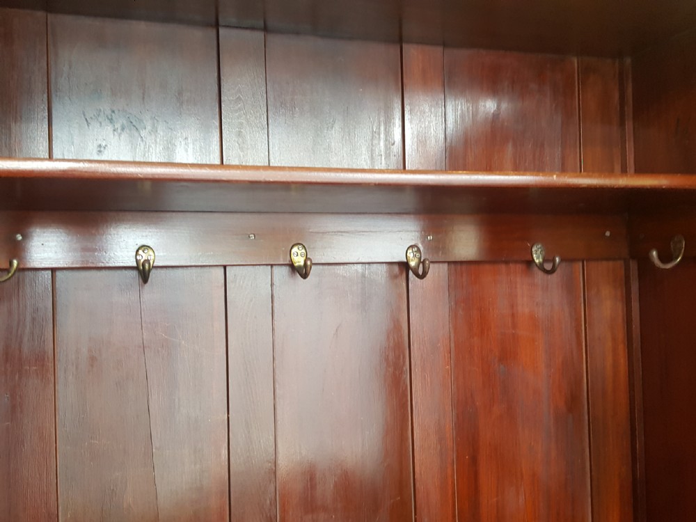 An Arts and Crafts mahogany hall robe featuring carved upper panels, two full-length doors, and a shaped top crest with corner finials. View XI