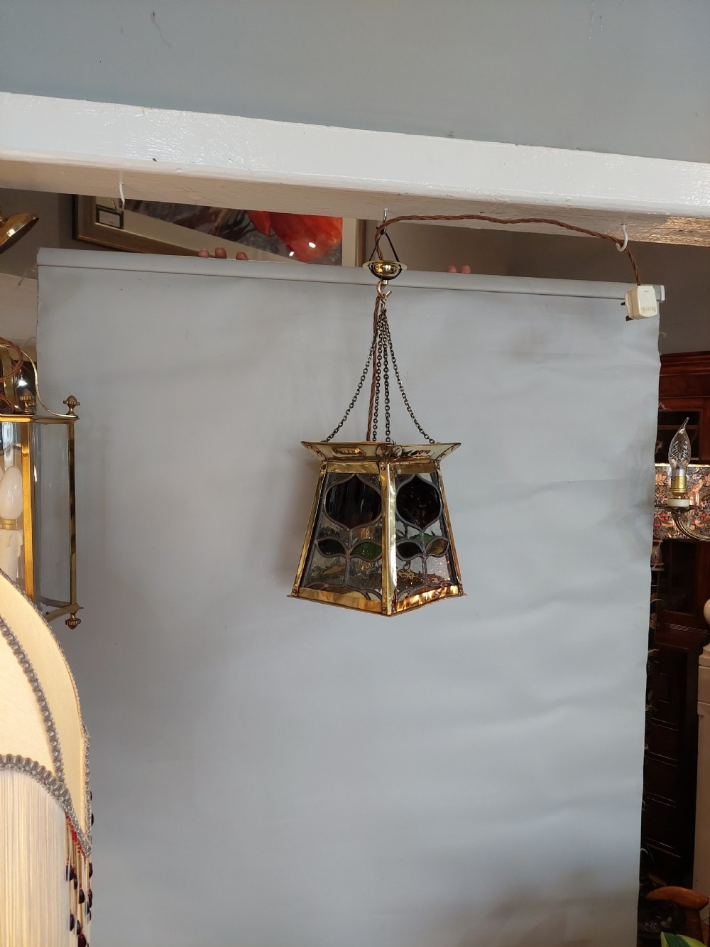An Arts and Crafts style brass pendant lantern featuring tapered sides, suspension chains, and leaded stained glass panels decorated with stylized botanical motifs. View II