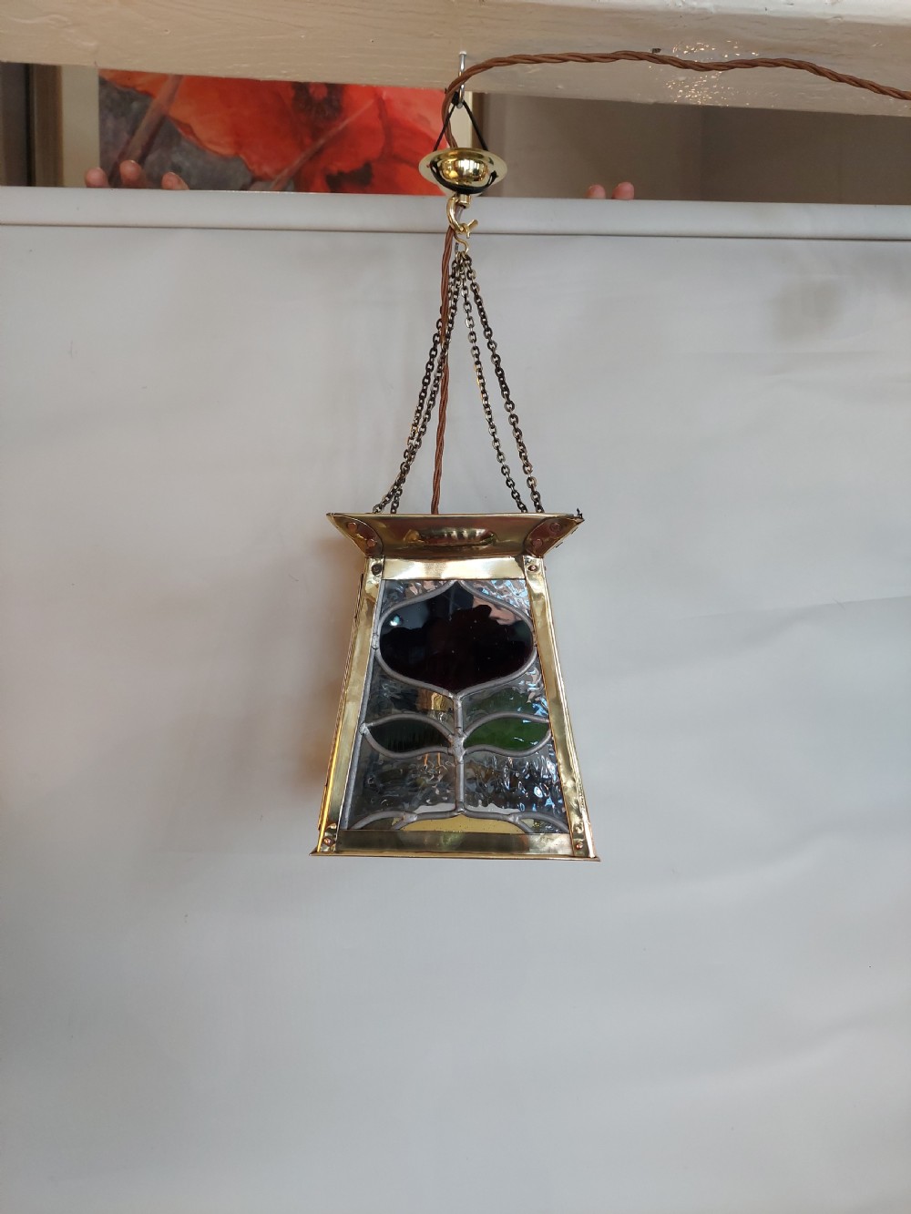 An Arts and Crafts style brass pendant lantern featuring tapered sides, suspension chains, and leaded stained glass panels decorated with stylized botanical motifs. View IV