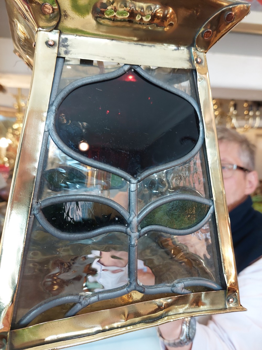 An Arts and Crafts style brass pendant lantern featuring tapered sides, suspension chains, and leaded stained glass panels decorated with stylized botanical motifs. View VI