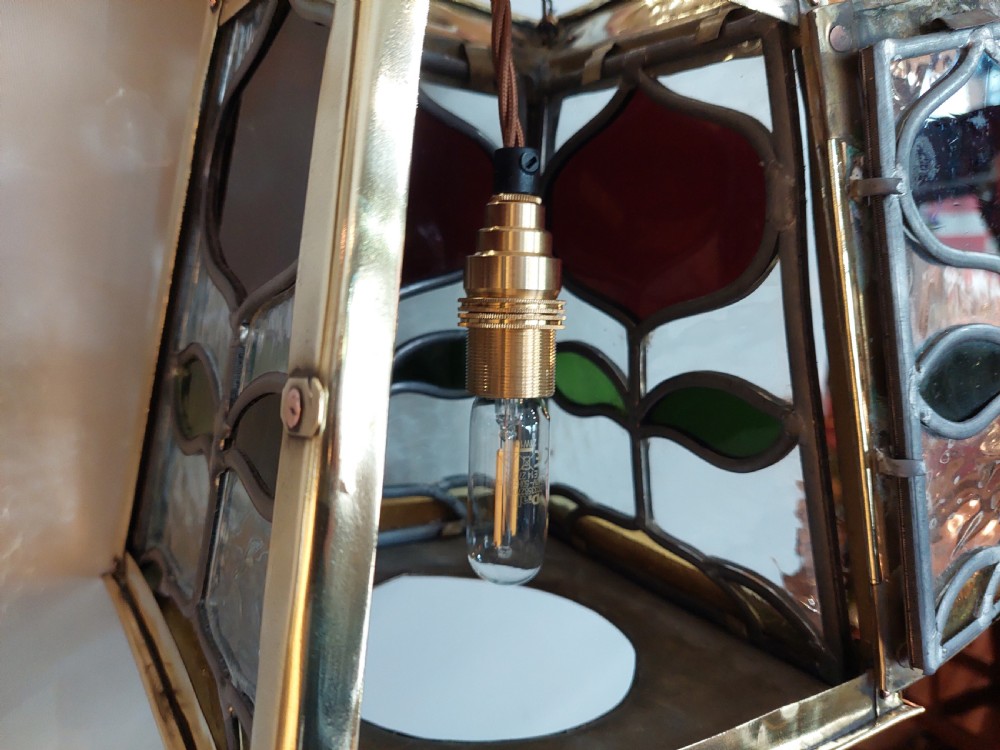 An Arts and Crafts style brass pendant lantern featuring tapered sides, suspension chains, and leaded stained glass panels decorated with stylized botanical motifs. View VIII