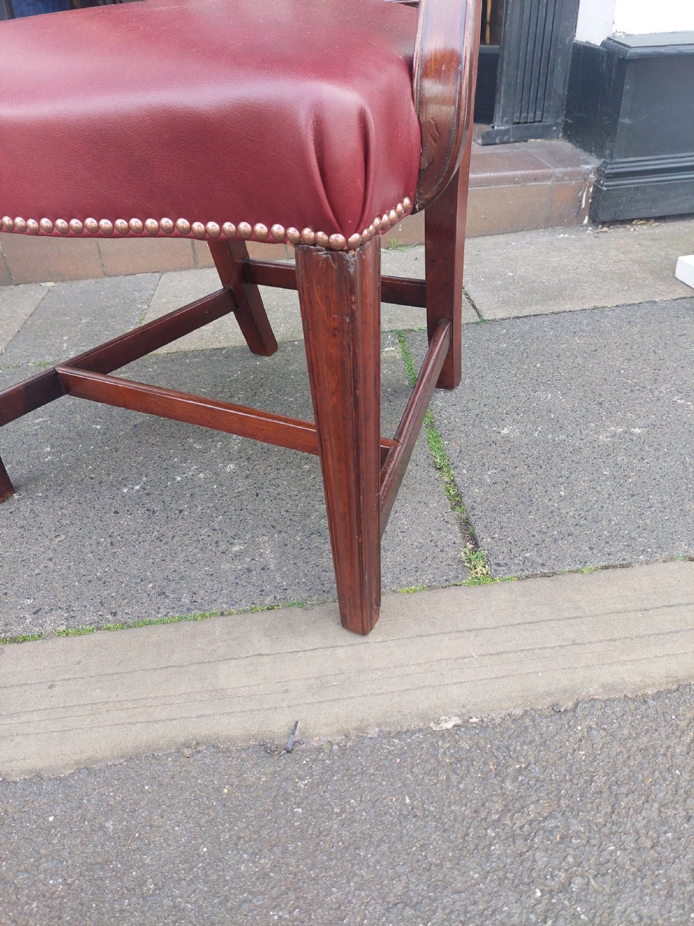A George III mahogany carver chair featuring vertical fluted back slats, curved armrests, and a red leather seat secured with brass studding. View V