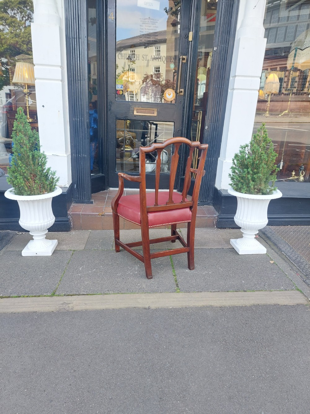 A George III mahogany carver chair featuring vertical fluted back slats, curved armrests, and a red leather seat secured with brass studding. View X