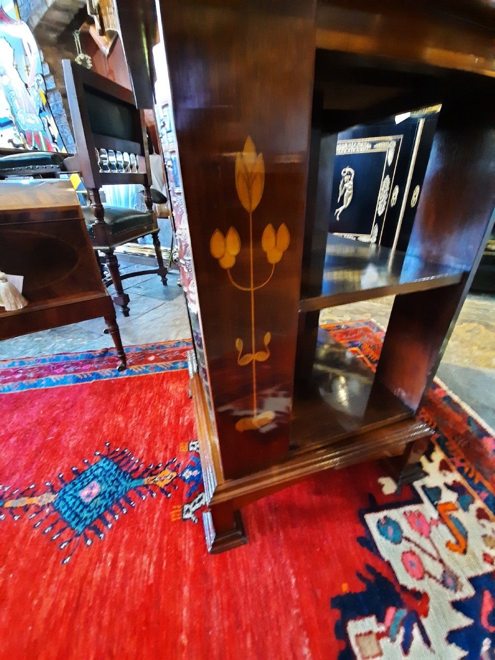 An Art Nouveau mahogany revolving bookcase featuring floral marquetry inlay on the side panel and two open tier shelves filled with leather-bound books. View II