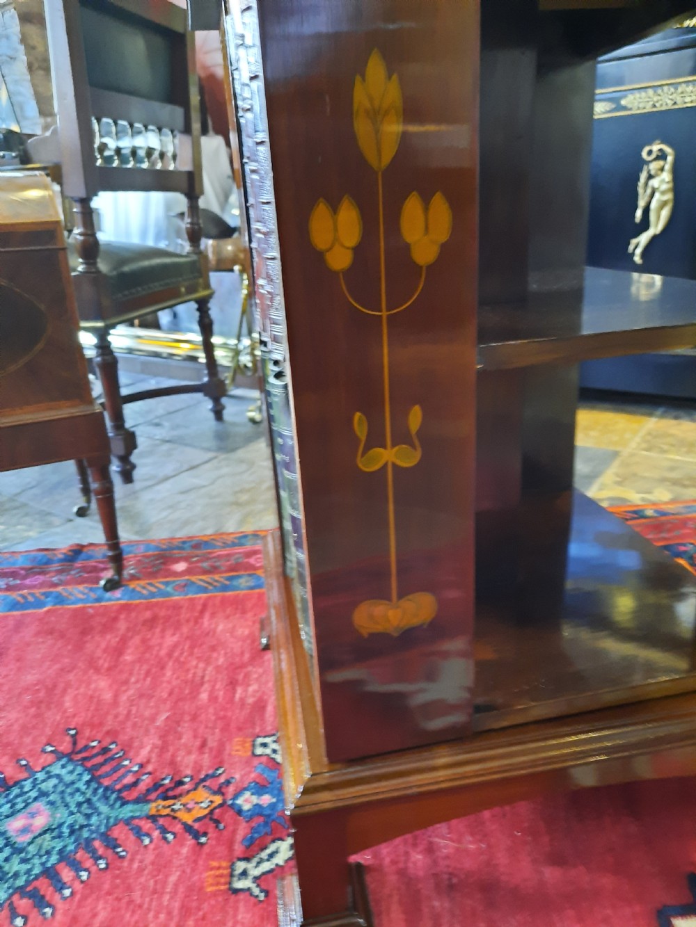 An Art Nouveau mahogany revolving bookcase featuring floral marquetry inlay on the side panel and two open tier shelves filled with leather-bound books. View III
