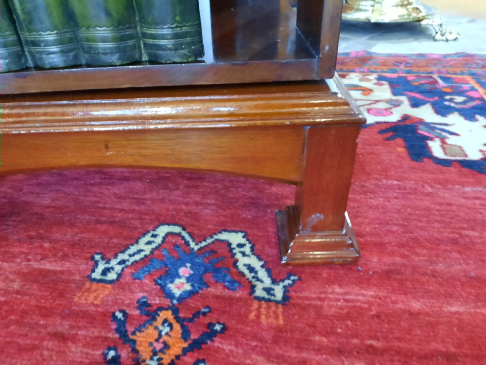 An Art Nouveau mahogany revolving bookcase featuring floral marquetry inlay on the side panel and two open tier shelves filled with leather-bound books. View V