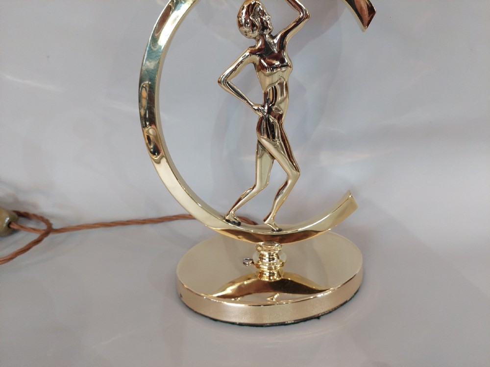 An Art Deco polished brass table lamp featuring a stylized female figure within a crescent frame supporting a pink frosted glass bowl shade. View III