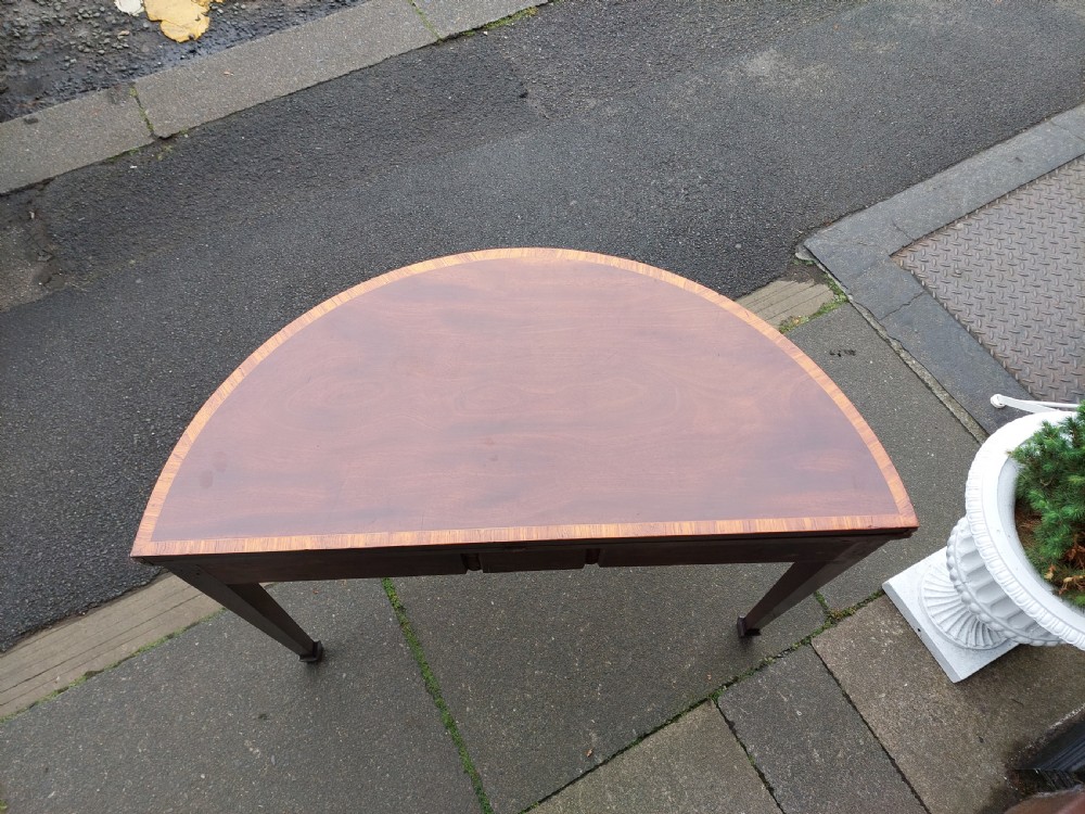 A George III mahogany demi-lune tea table featuring a fold-over top with crossbanded inlay and square tapered legs. View III