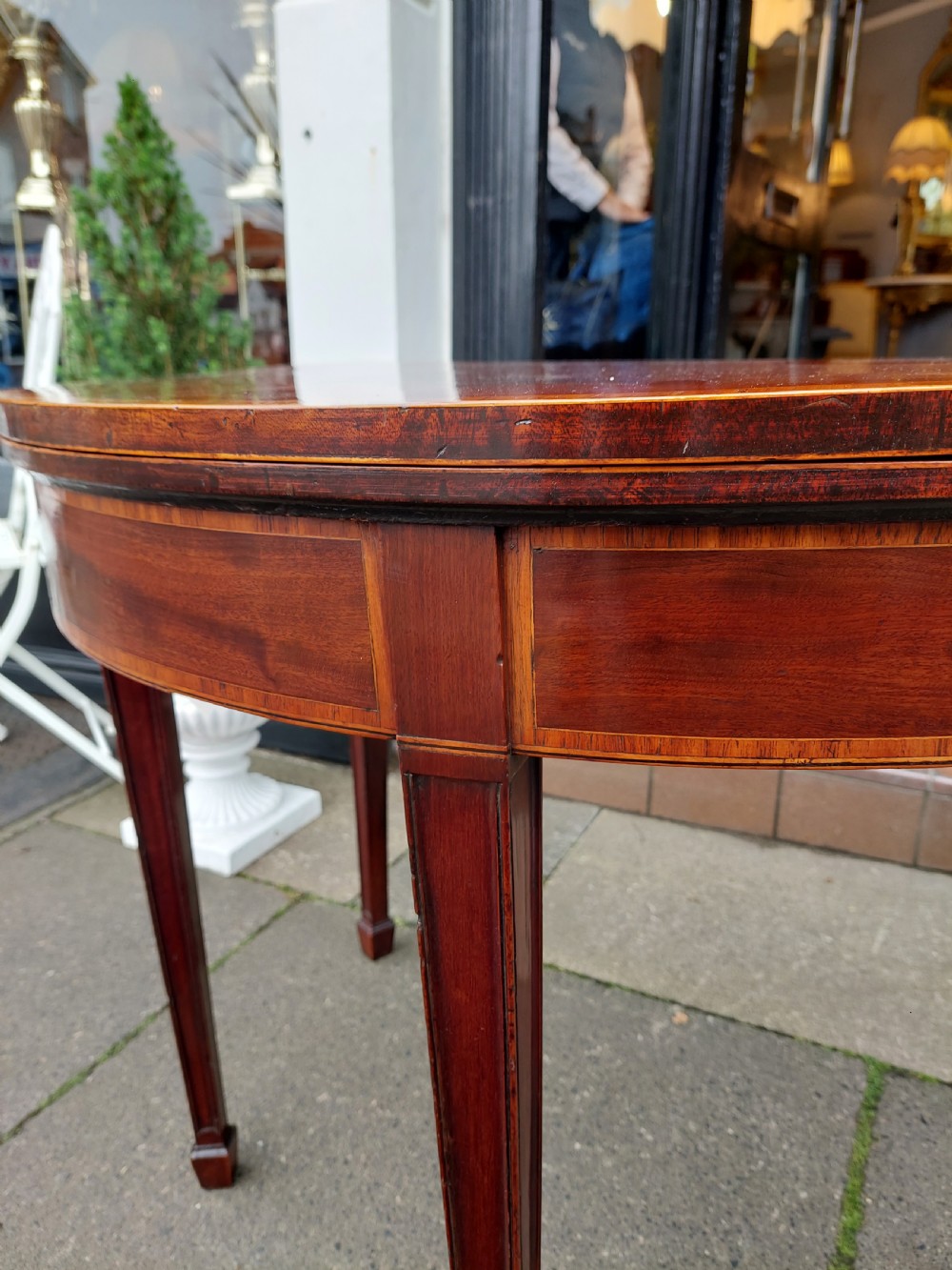 A George III mahogany demi-lune tea table featuring a fold-over top with crossbanded inlay and square tapered legs. View V