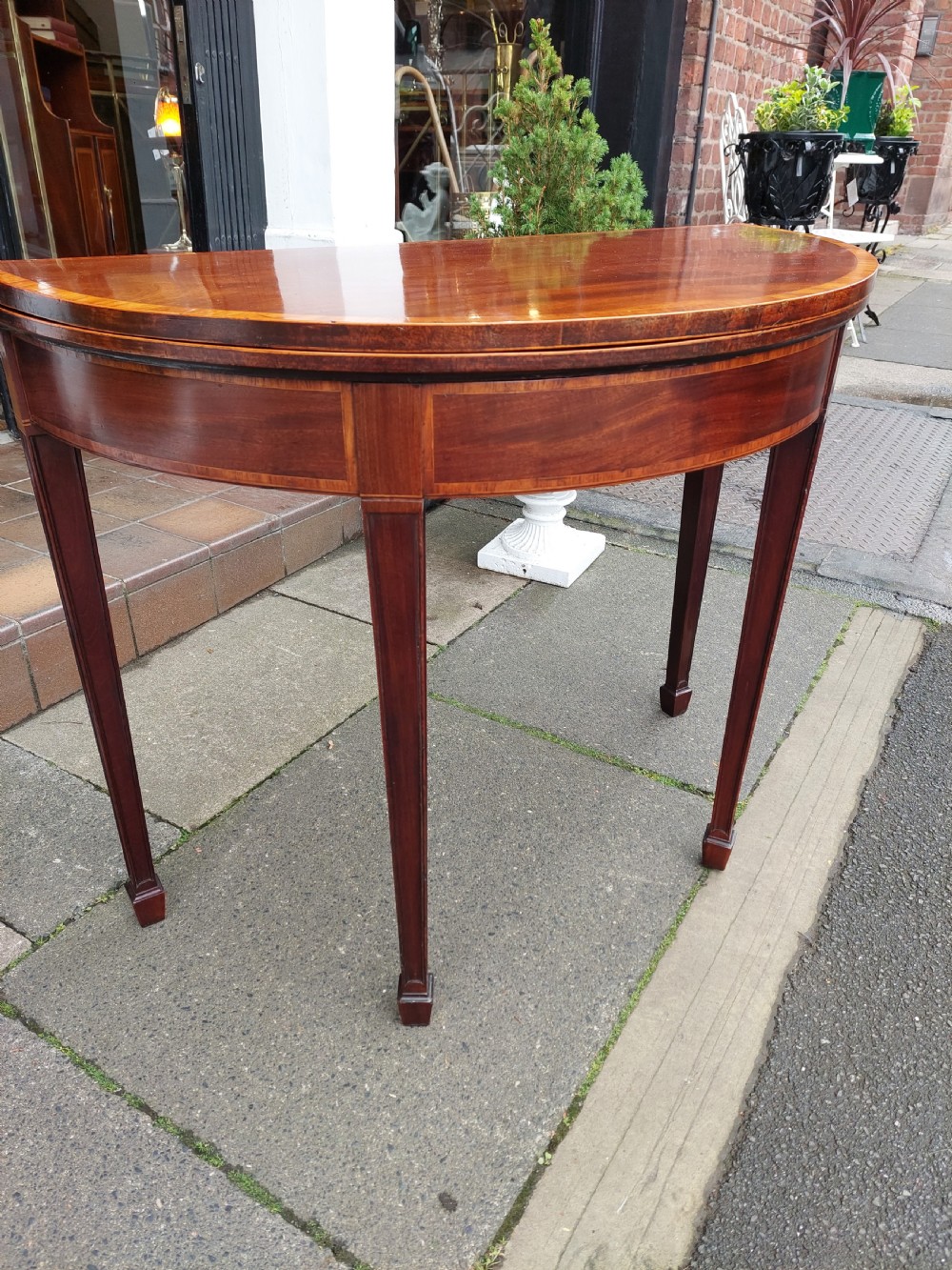 A George III mahogany demi-lune tea table featuring a fold-over top with crossbanded inlay and square tapered legs. View VII