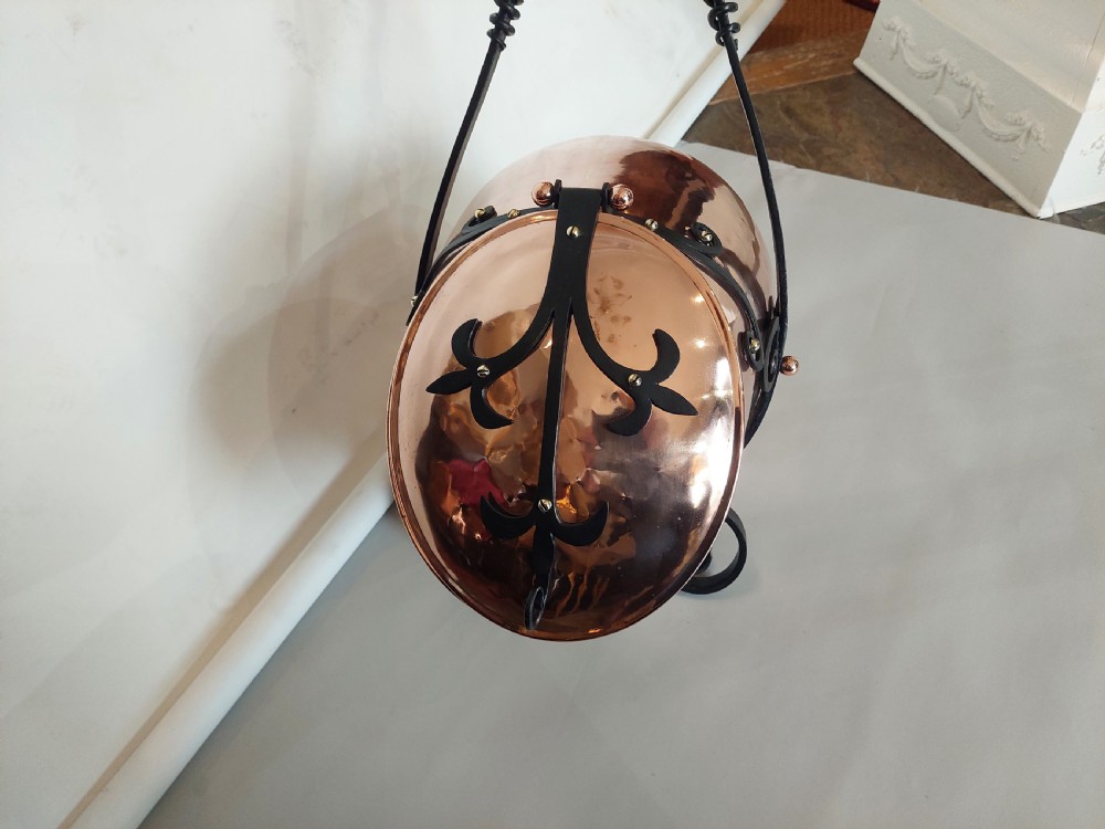 A hand-hammered copper coal receiver supported by a black wrought iron frame with scroll feet and an elevated handle. View III