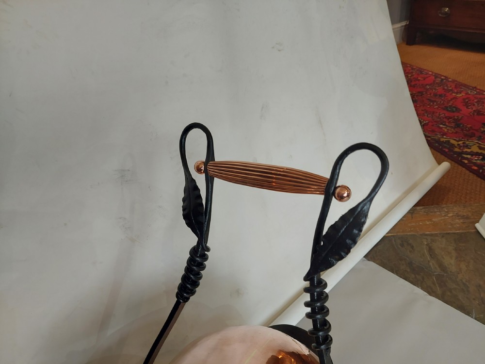 A hand-hammered copper coal receiver supported by a black wrought iron frame with scroll feet and an elevated handle. View IV