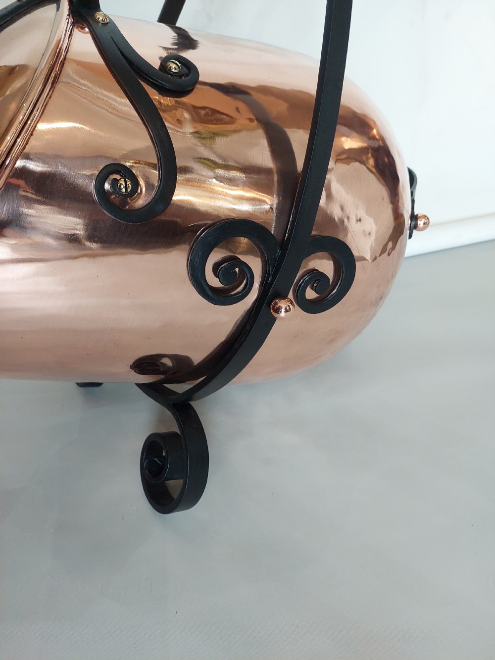 A hand-hammered copper coal receiver supported by a black wrought iron frame with scroll feet and an elevated handle. View V