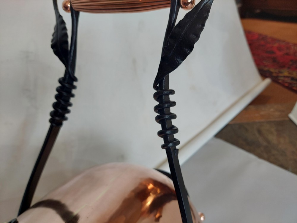 A hand-hammered copper coal receiver supported by a black wrought iron frame with scroll feet and an elevated handle. View VI
