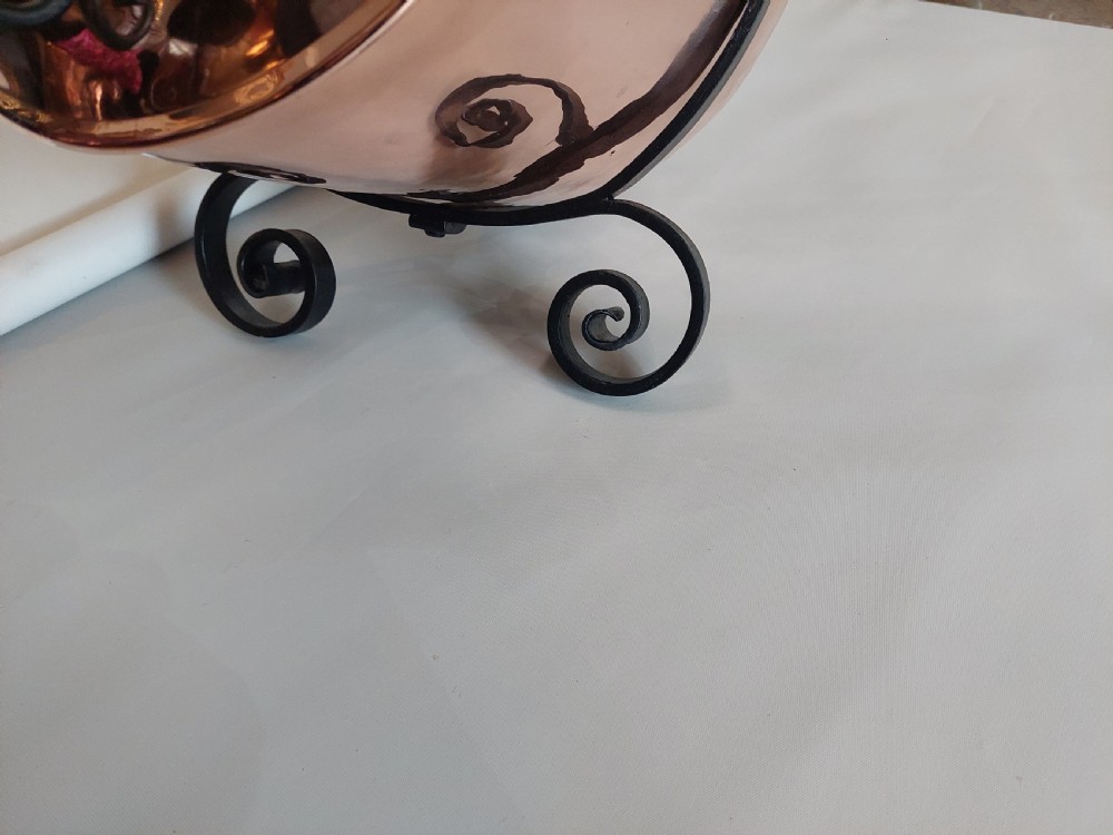 A hand-hammered copper coal receiver supported by a black wrought iron frame with scroll feet and an elevated handle. View VII