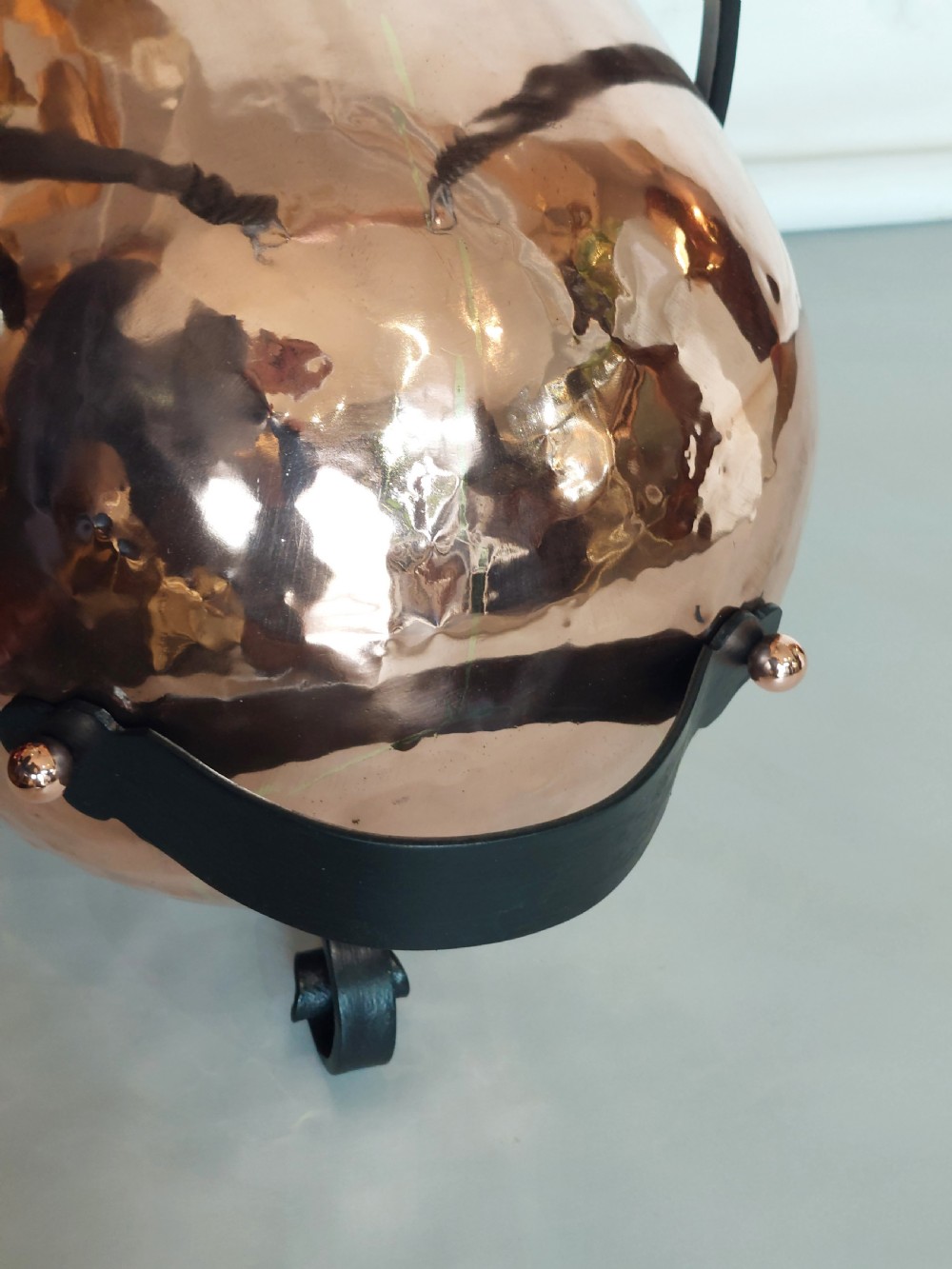 A hand-hammered copper coal receiver supported by a black wrought iron frame with scroll feet and an elevated handle. View IX