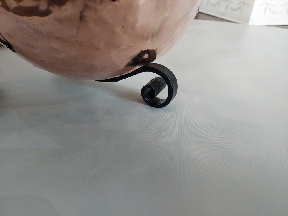 A hand-hammered copper coal receiver supported by a black wrought iron frame with scroll feet and an elevated handle. View XI