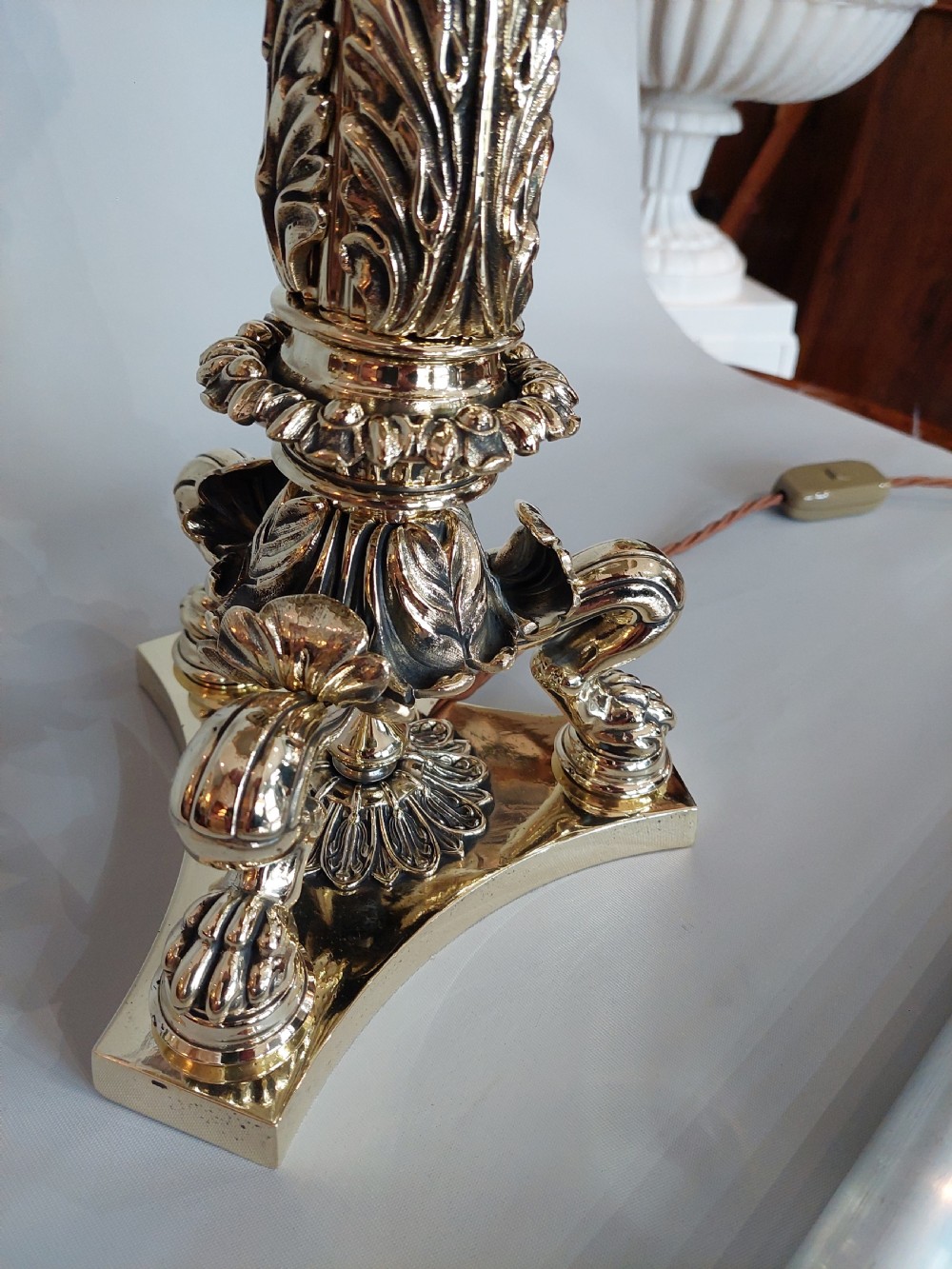 A Victorian brass table lamp featuring a columned base with acanthus leaf moulding and a cream fabric lampshade trimmed with burgundy fringe. View III