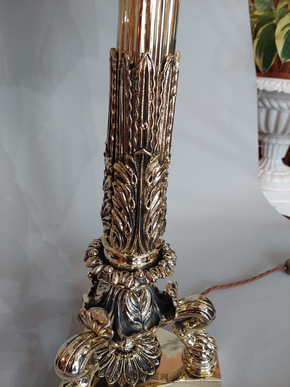 A Victorian brass table lamp featuring a columned base with acanthus leaf moulding and a cream fabric lampshade trimmed with burgundy fringe. View IV