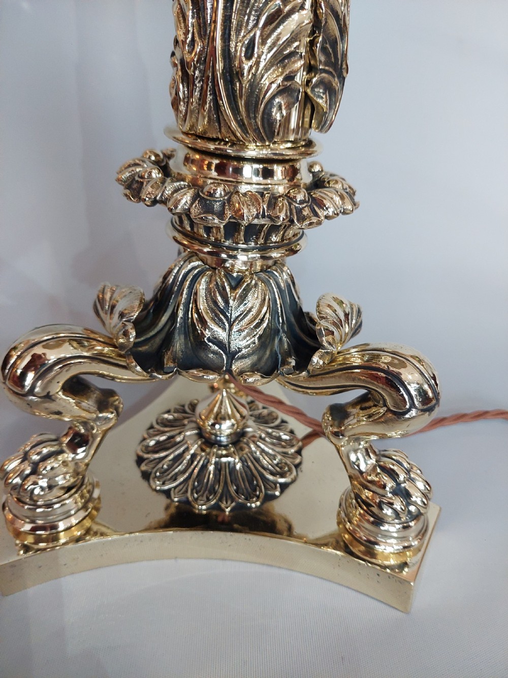 A Victorian brass table lamp featuring a columned base with acanthus leaf moulding and a cream fabric lampshade trimmed with burgundy fringe. View VI