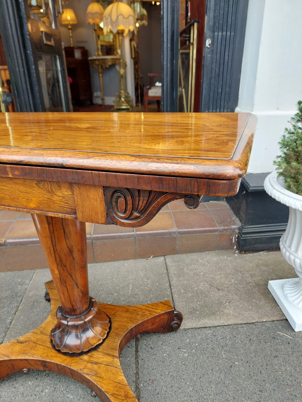 A William IV rosewood card table featuring a rectangular swivel top resting on a tapered column pedestal and a concave quadform plinth base with scroll feet. View III