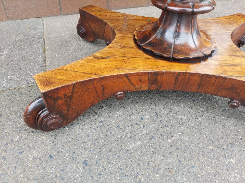 A William IV rosewood card table featuring a rectangular swivel top resting on a tapered column pedestal and a concave quadform plinth base with scroll feet. View IV