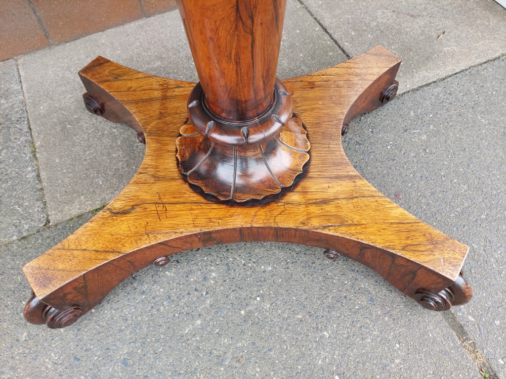 A William IV rosewood card table featuring a rectangular swivel top resting on a tapered column pedestal and a concave quadform plinth base with scroll feet. View VI