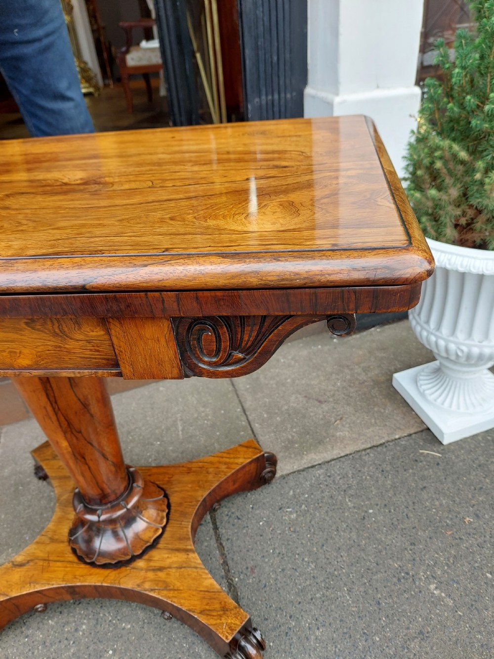A William IV rosewood card table featuring a rectangular swivel top resting on a tapered column pedestal and a concave quadform plinth base with scroll feet. View VII