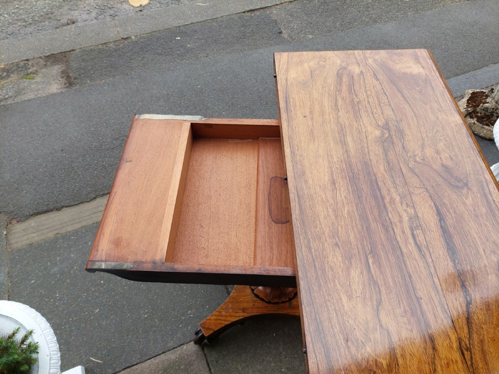A William IV rosewood card table featuring a rectangular swivel top resting on a tapered column pedestal and a concave quadform plinth base with scroll feet. View X