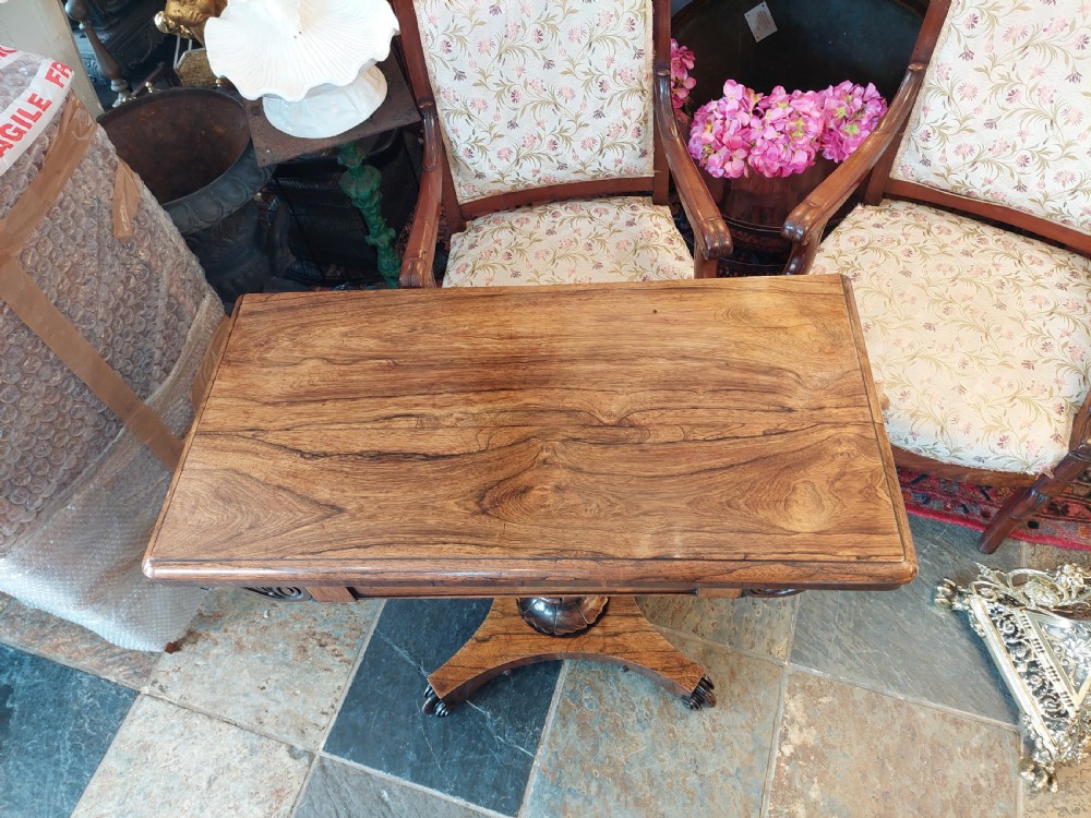 A William IV rosewood card table featuring a rectangular swivel top resting on a tapered column pedestal and a concave quadform plinth base with scroll feet. View XI
