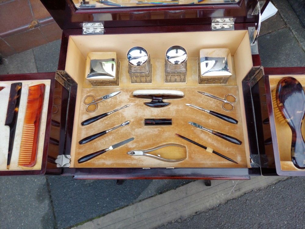 An early twentieth-century mahogany gentlemans vanity table featuring a hinged top mirror and side compartments displaying glass bottles and grooming accessories. View III