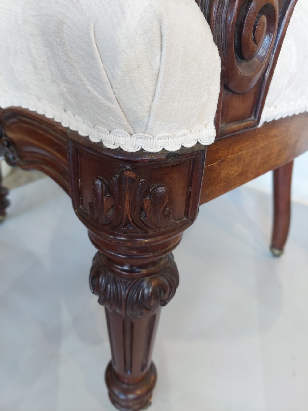 An antique Regency carved mahogany armchair upholstered in cream damask fabric, featuring scroll arms and turned front legs with castors. View III