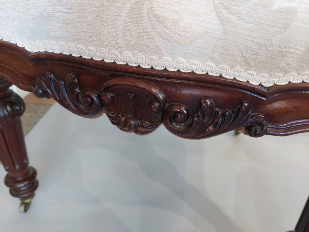 An antique Regency carved mahogany armchair upholstered in cream damask fabric, featuring scroll arms and turned front legs with castors. View VI