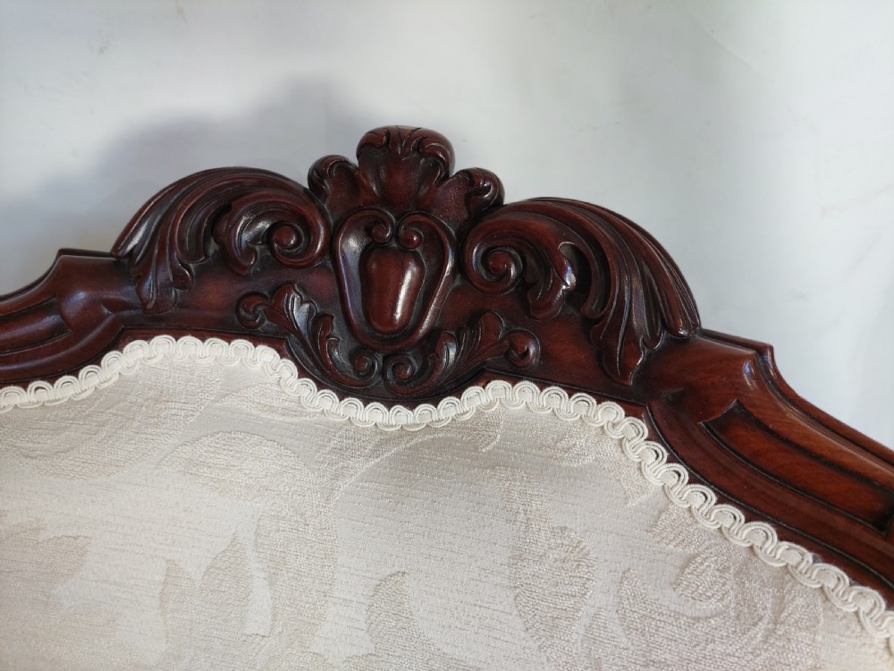 An antique Regency carved mahogany armchair upholstered in cream damask fabric, featuring scroll arms and turned front legs with castors. View VII