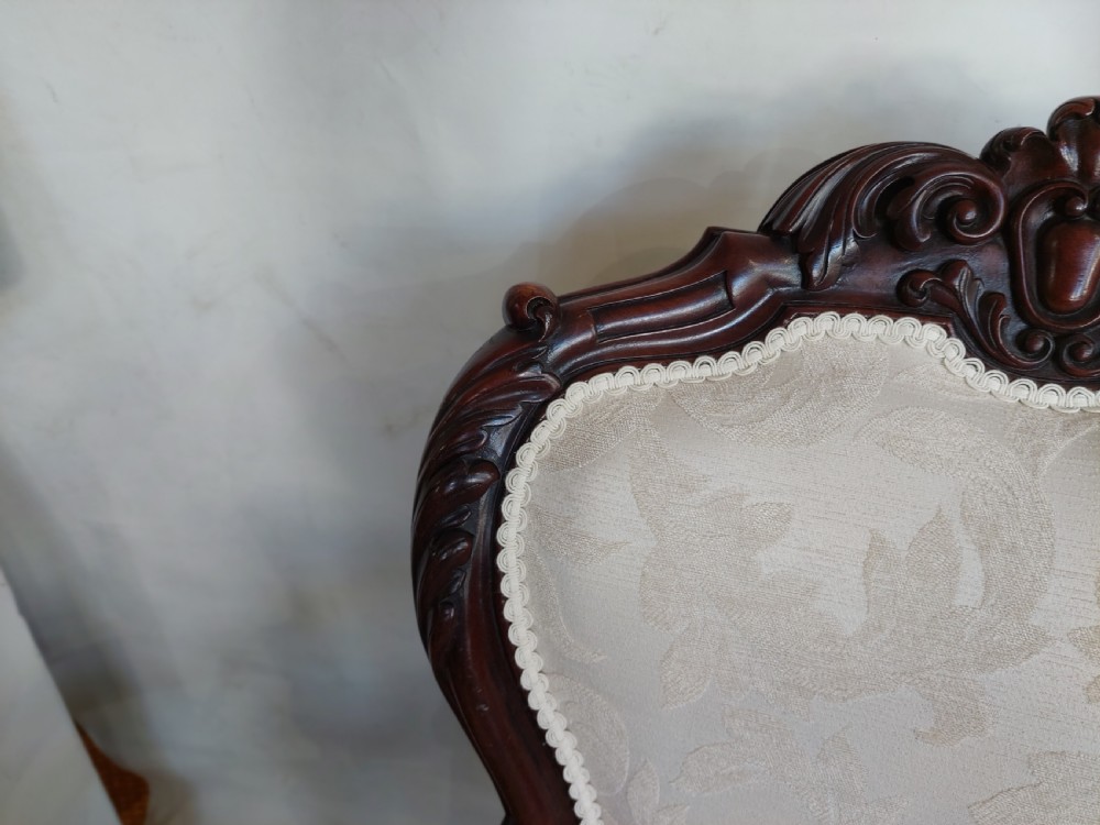 An antique Regency carved mahogany armchair upholstered in cream damask fabric, featuring scroll arms and turned front legs with castors. View VIII