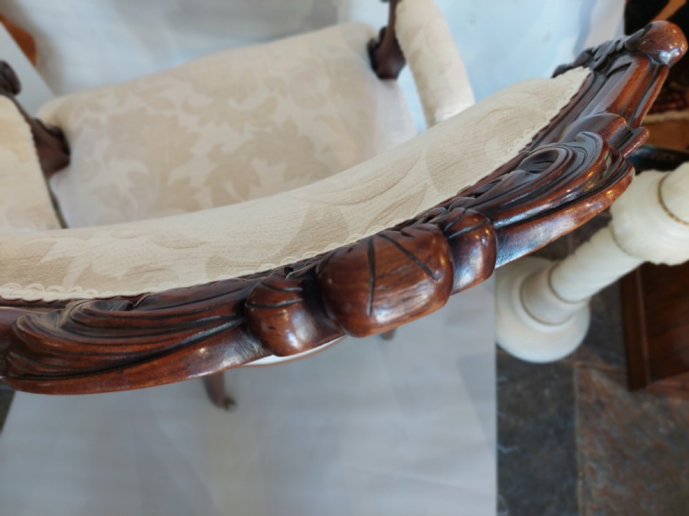 An antique Regency carved mahogany armchair upholstered in cream damask fabric, featuring scroll arms and turned front legs with castors. View IX