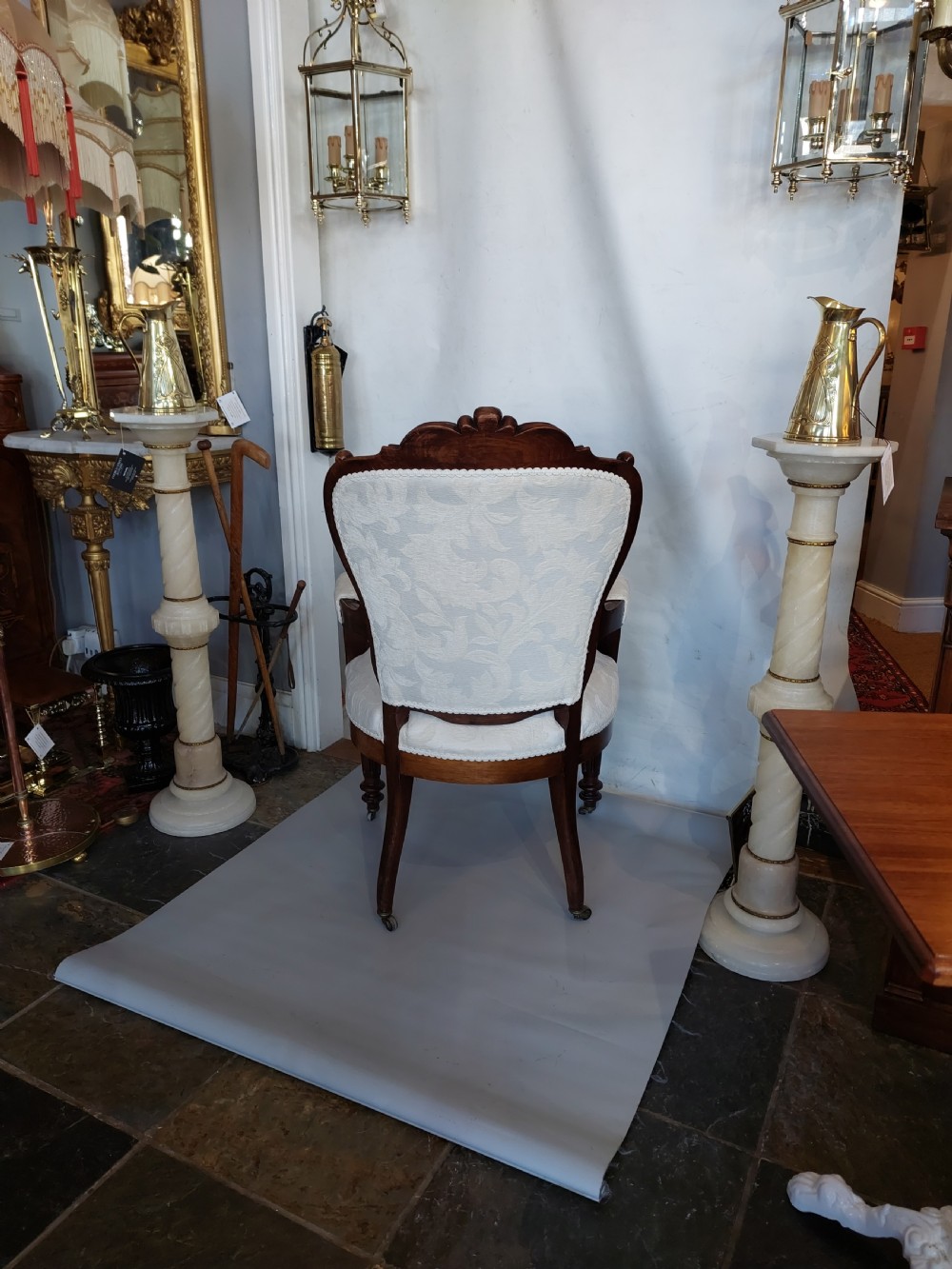 An antique Regency carved mahogany armchair upholstered in cream damask fabric, featuring scroll arms and turned front legs with castors. View X
