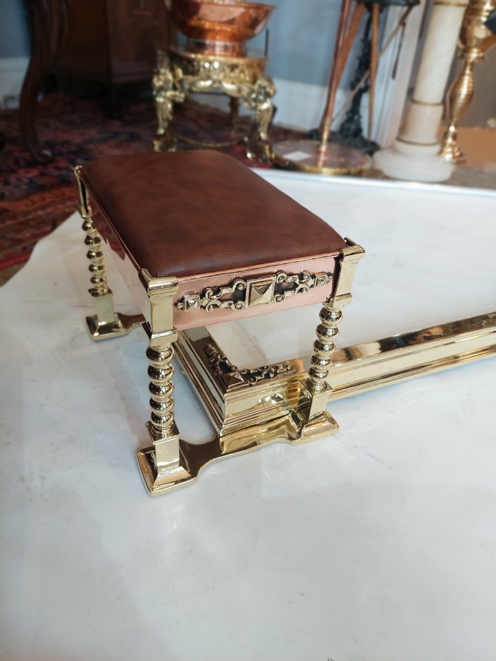A Victorian brass and copper club fender featuring two padded brown leather corner seats raised on turned brass supports with decorative metal frieze detail. View II