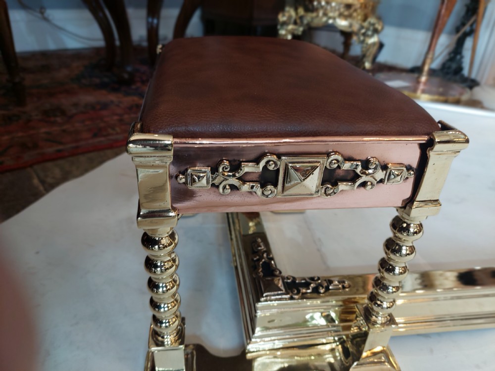 A Victorian brass and copper club fender featuring two padded brown leather corner seats raised on turned brass supports with decorative metal frieze detail. View IV
