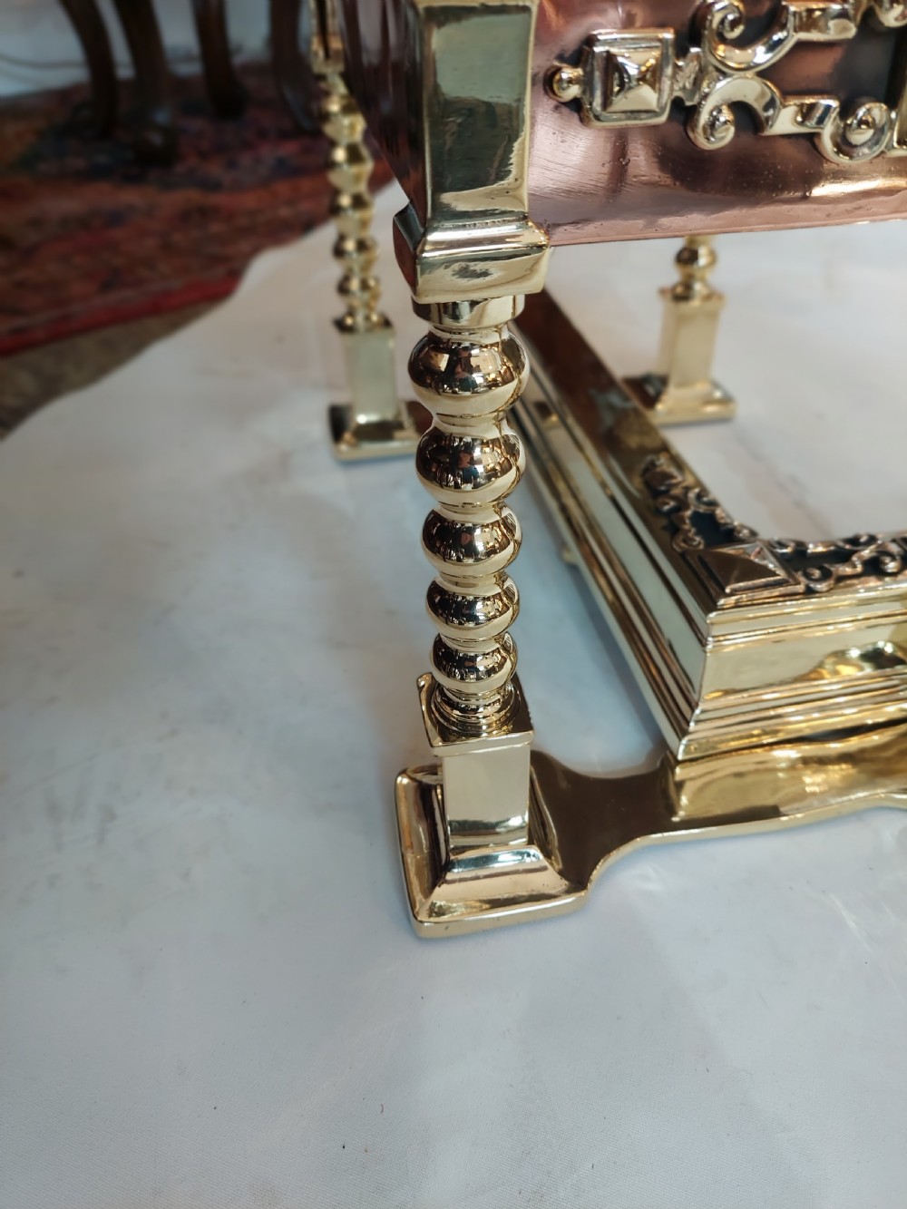 A Victorian brass and copper club fender featuring two padded brown leather corner seats raised on turned brass supports with decorative metal frieze detail. View V