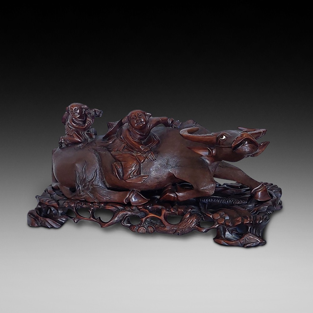 A 19th-century Chinese carved root wood sculpture depicting two boys riding a reclining water buffalo set upon a carved pierced base.