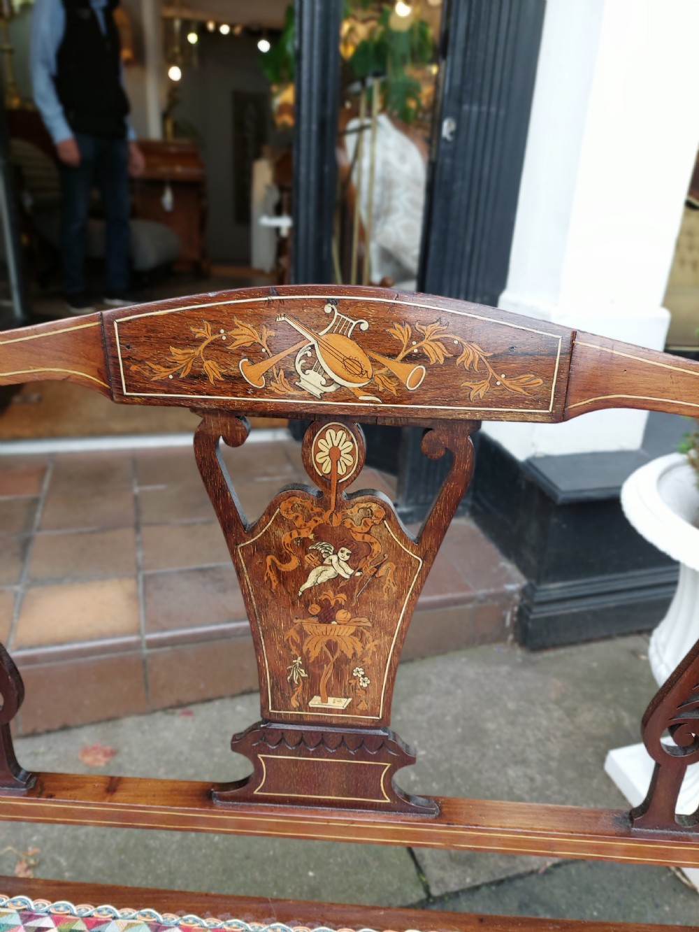 An Edwardian mahogany two-seater settee with decorative central marquetry splats, curved arms, splayed legs, and colourful geometric upholstery. View II