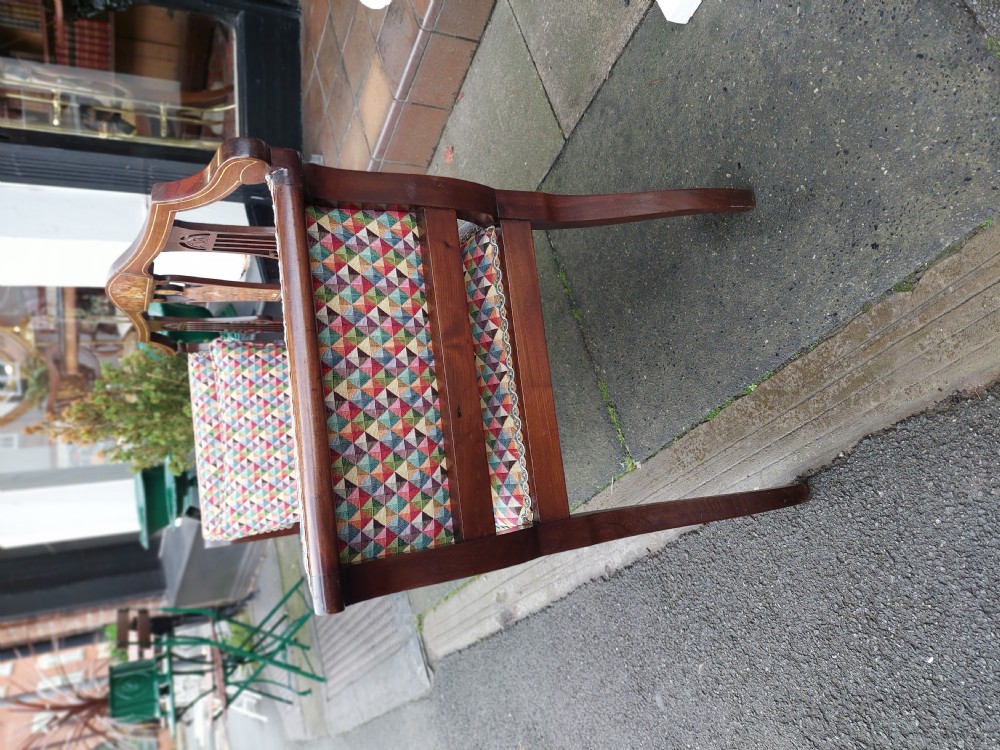 An Edwardian mahogany two-seater settee with decorative central marquetry splats, curved arms, splayed legs, and colourful geometric upholstery. View VI
