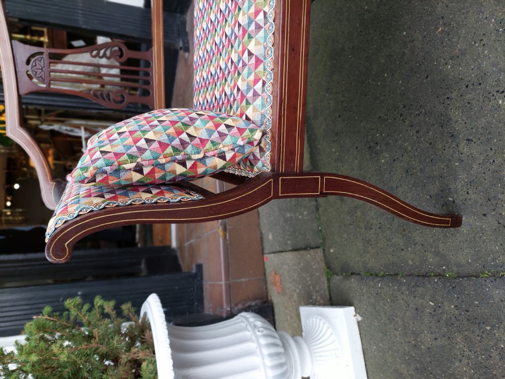 An Edwardian mahogany two-seater settee with decorative central marquetry splats, curved arms, splayed legs, and colourful geometric upholstery. View VII