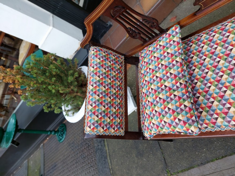 An Edwardian mahogany two-seater settee with decorative central marquetry splats, curved arms, splayed legs, and colourful geometric upholstery. View VIII