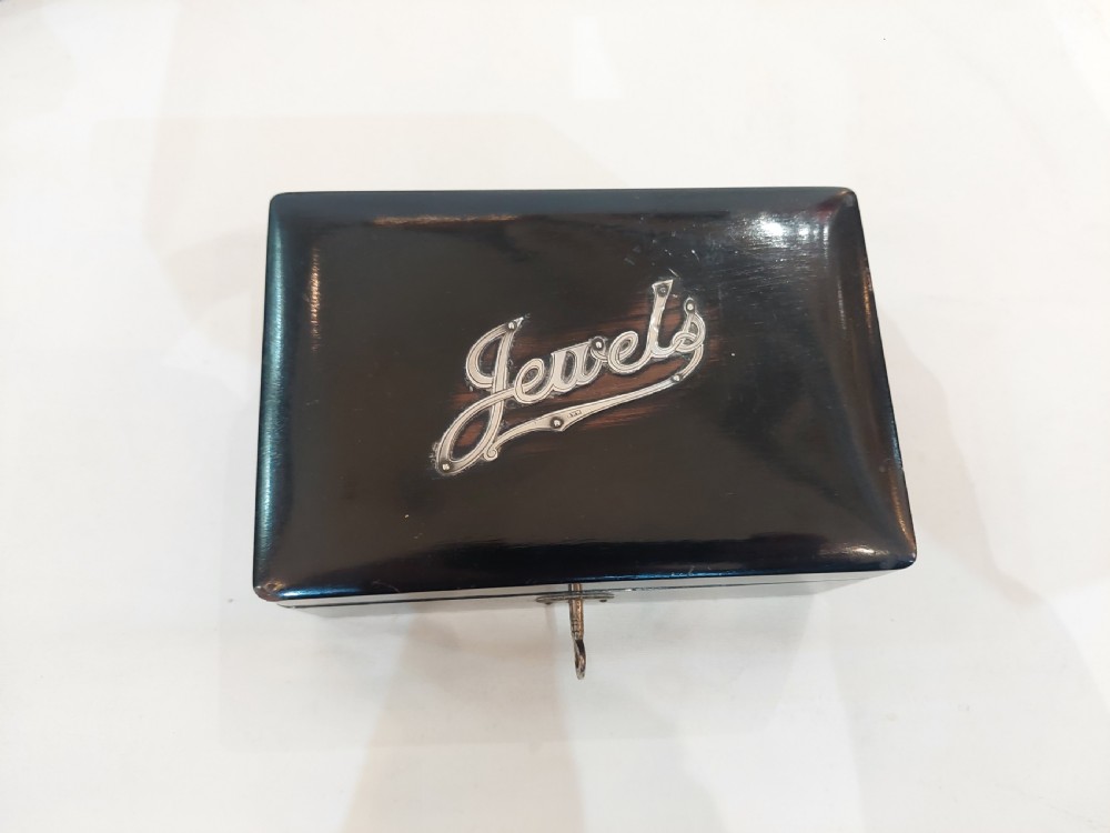 A rectangular black ebonised jewellery box with inlaid silver script alongside a matching tray featuring silver corner mounts. View IV