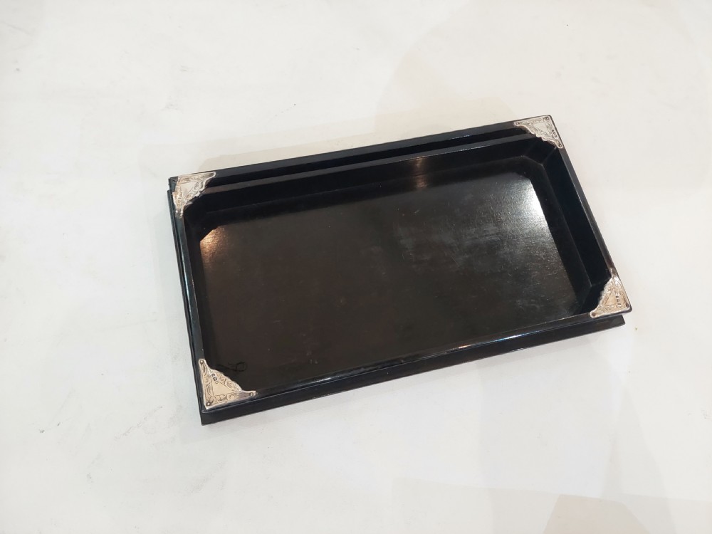 A rectangular black ebonised jewellery box with inlaid silver script alongside a matching tray featuring silver corner mounts. View V