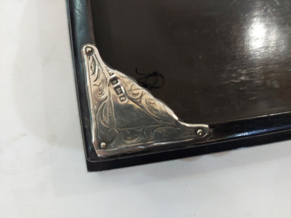 A rectangular black ebonised jewellery box with inlaid silver script alongside a matching tray featuring silver corner mounts. View VI